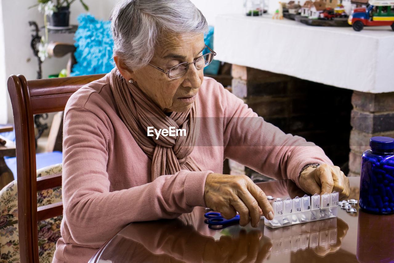 Senior woman taking medicine while sitting by table at home