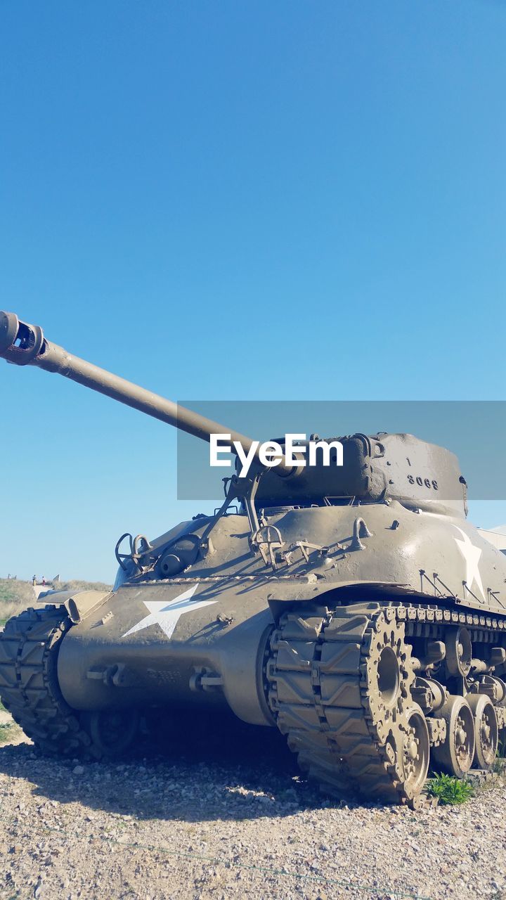 Armored tank on field against clear blue sky