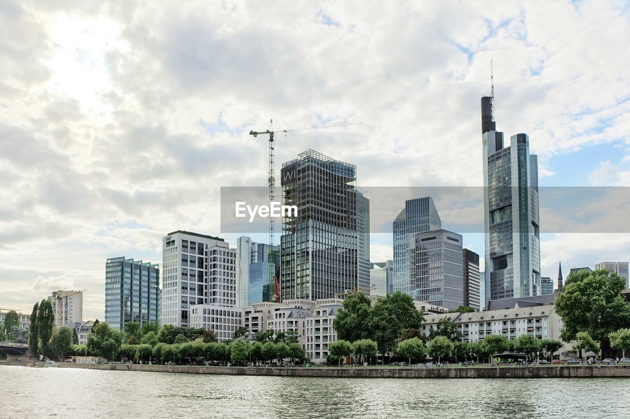 Modern cityscape by river against sky