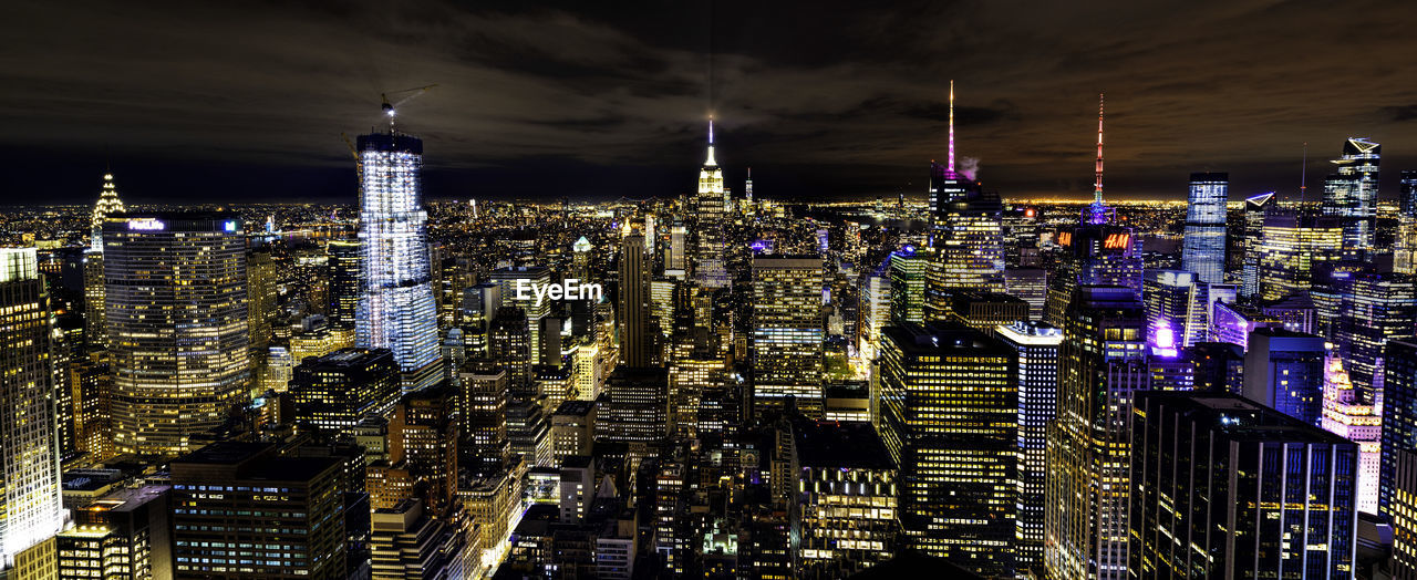 Illuminated modern buildings in city against sky at night