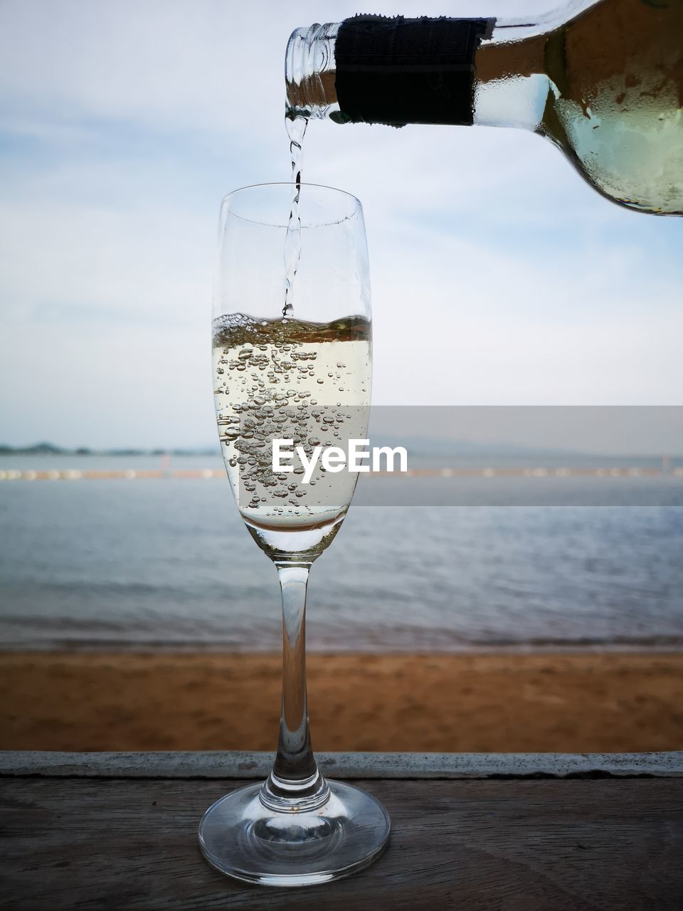 Pouring wine into a glass on table by sea against sky
