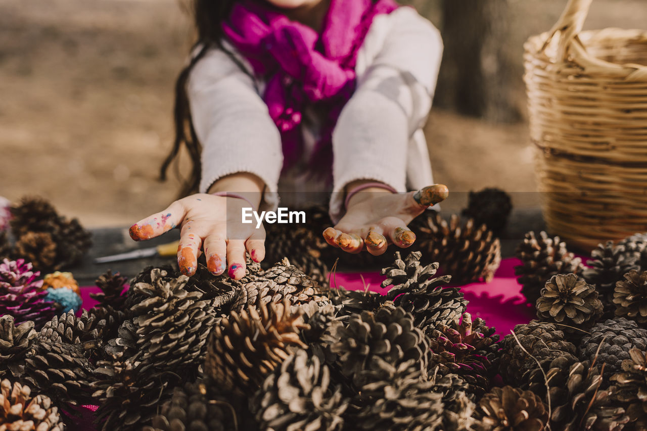 Messy hands of girl with pine cones at picnic table in park