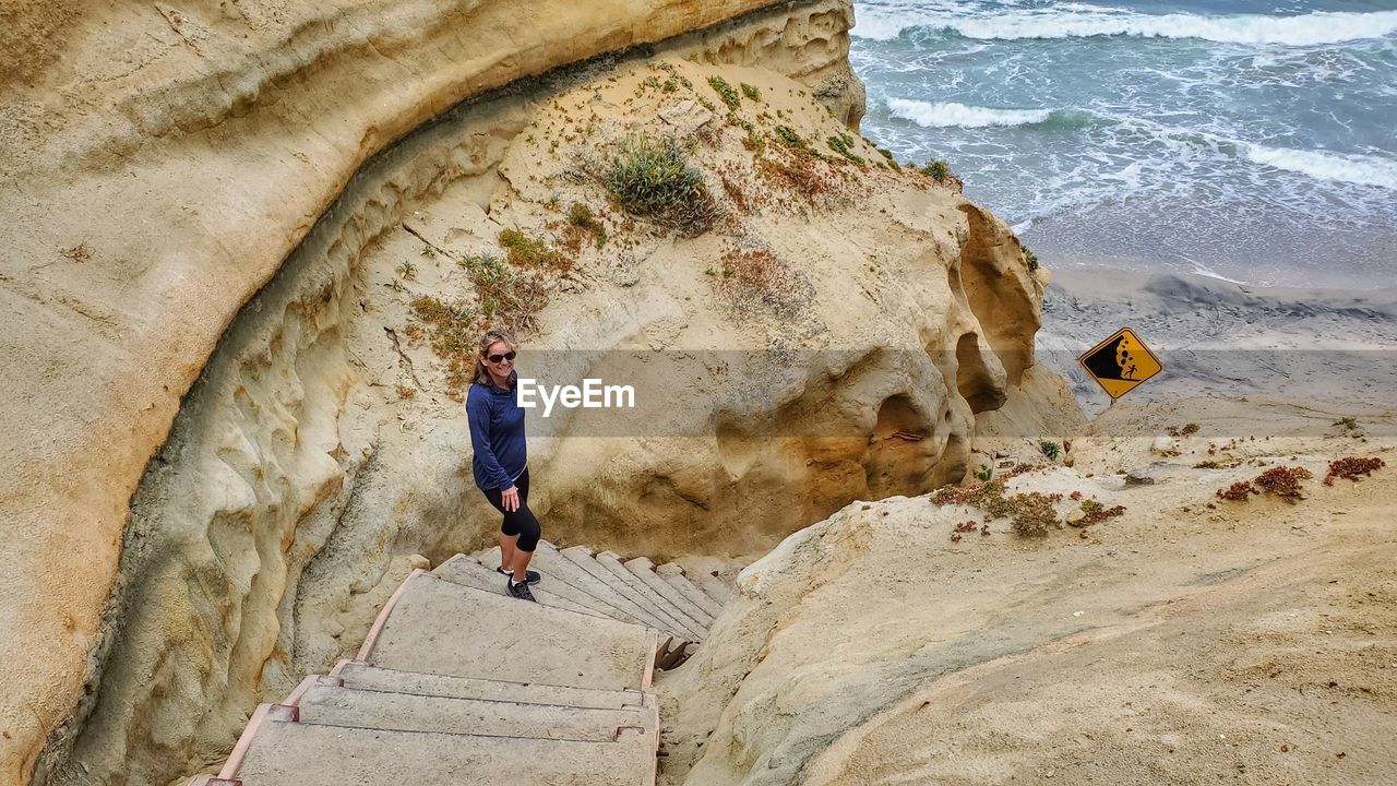 Full length of woman standing on staircase by rock formations at beach
