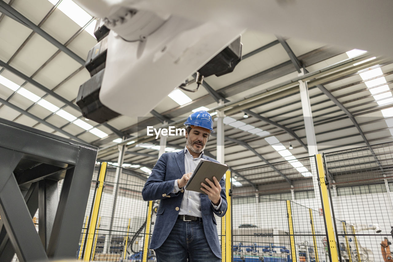 Engineer wearing hardhat using tablet pc in factory