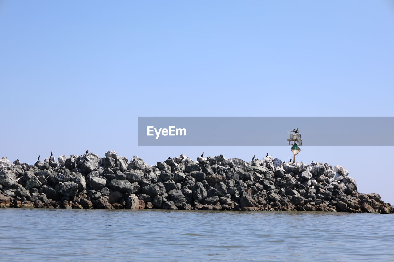 SEA BY ROCKS AGAINST CLEAR BLUE SKY
