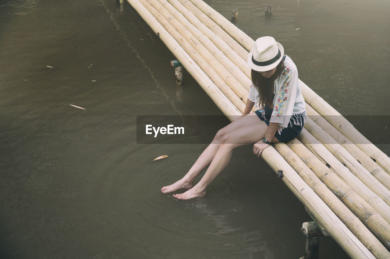 High angle view of young woman relaxing on footbridge over lake