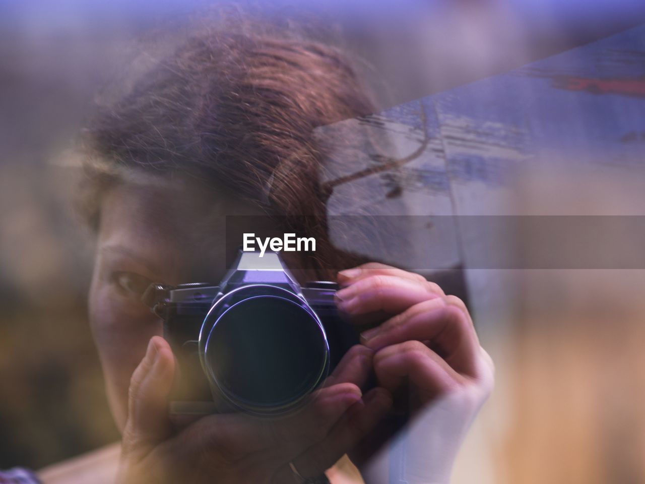 Woman photographing from camera seen through glass