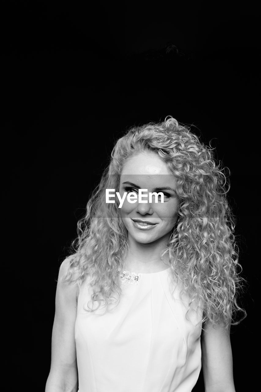 Woman with curly hair standing against black background