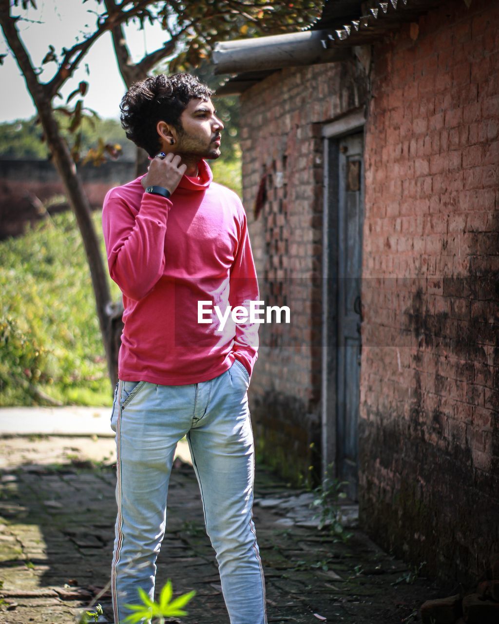 FULL LENGTH OF YOUNG MAN LOOKING AWAY WHILE STANDING AGAINST WALL