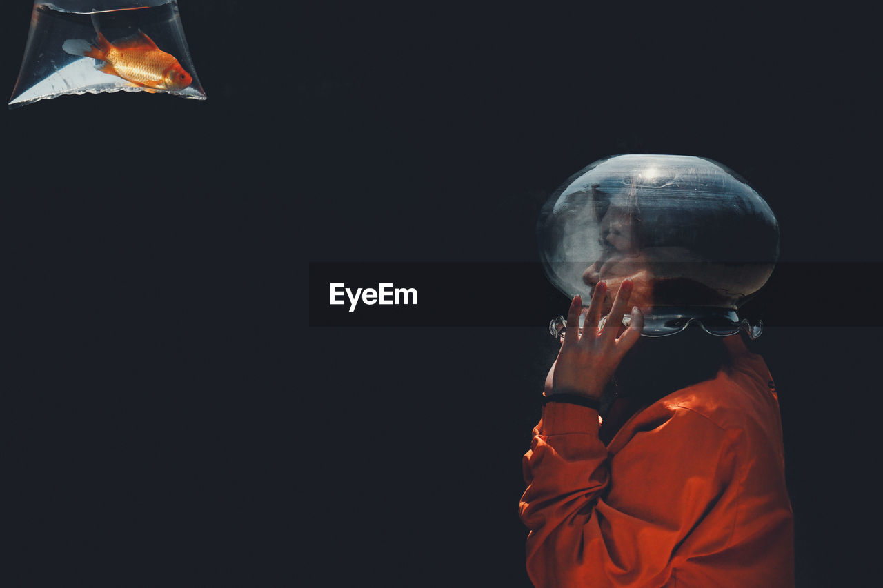 Side view of man wearing container on face while looking at fish against black background