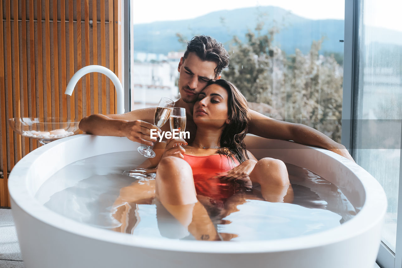 Couple having champagne while relaxing in bathtub at bathroom