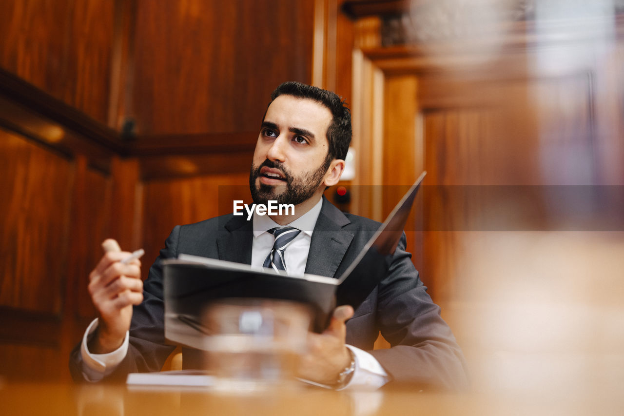 Confident bearded male lawyer with contract file sitting in board room during meeting