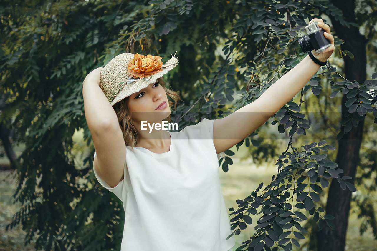 Woman taking selfie through camera against trees
