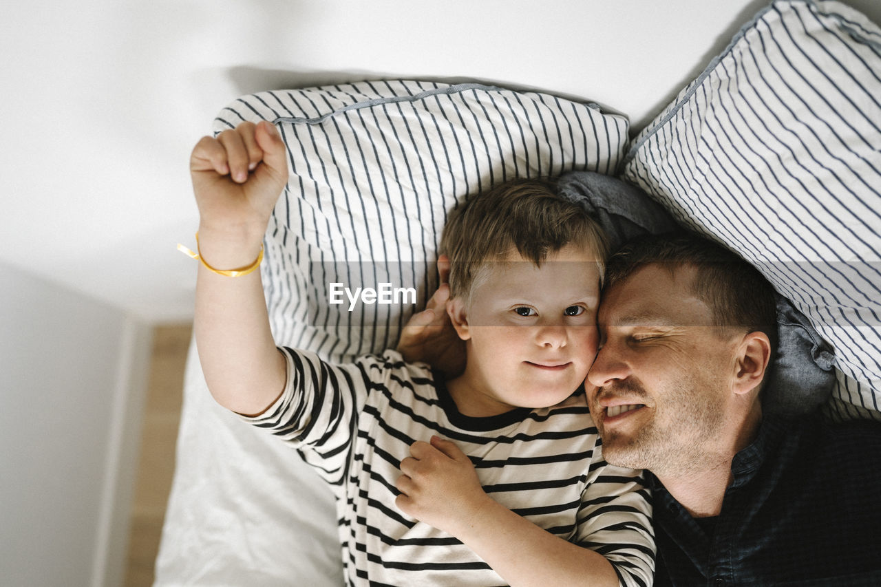 Directly above shot of father and son resting on bed in bedroom