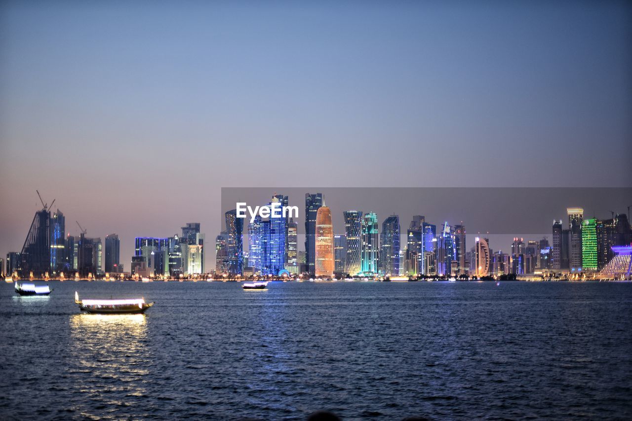 Sea by illuminated buildings against clear sky