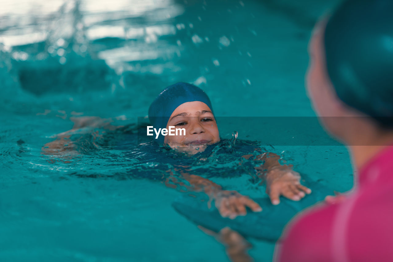 Boy learning to swim in pool with teacher