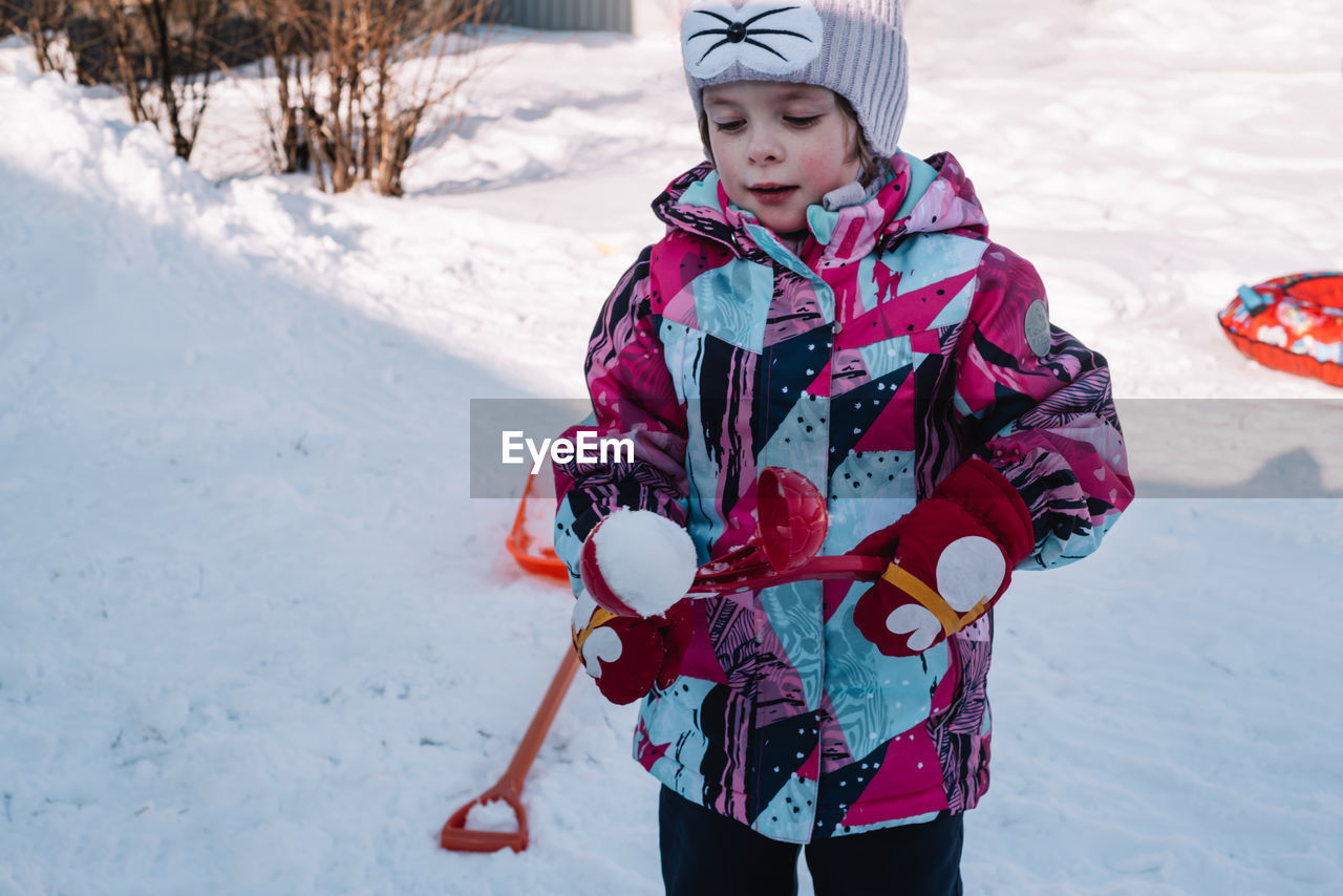 Happy and cheerful child in winter, in snowy weather, makes snowballs out of snow. hello winter