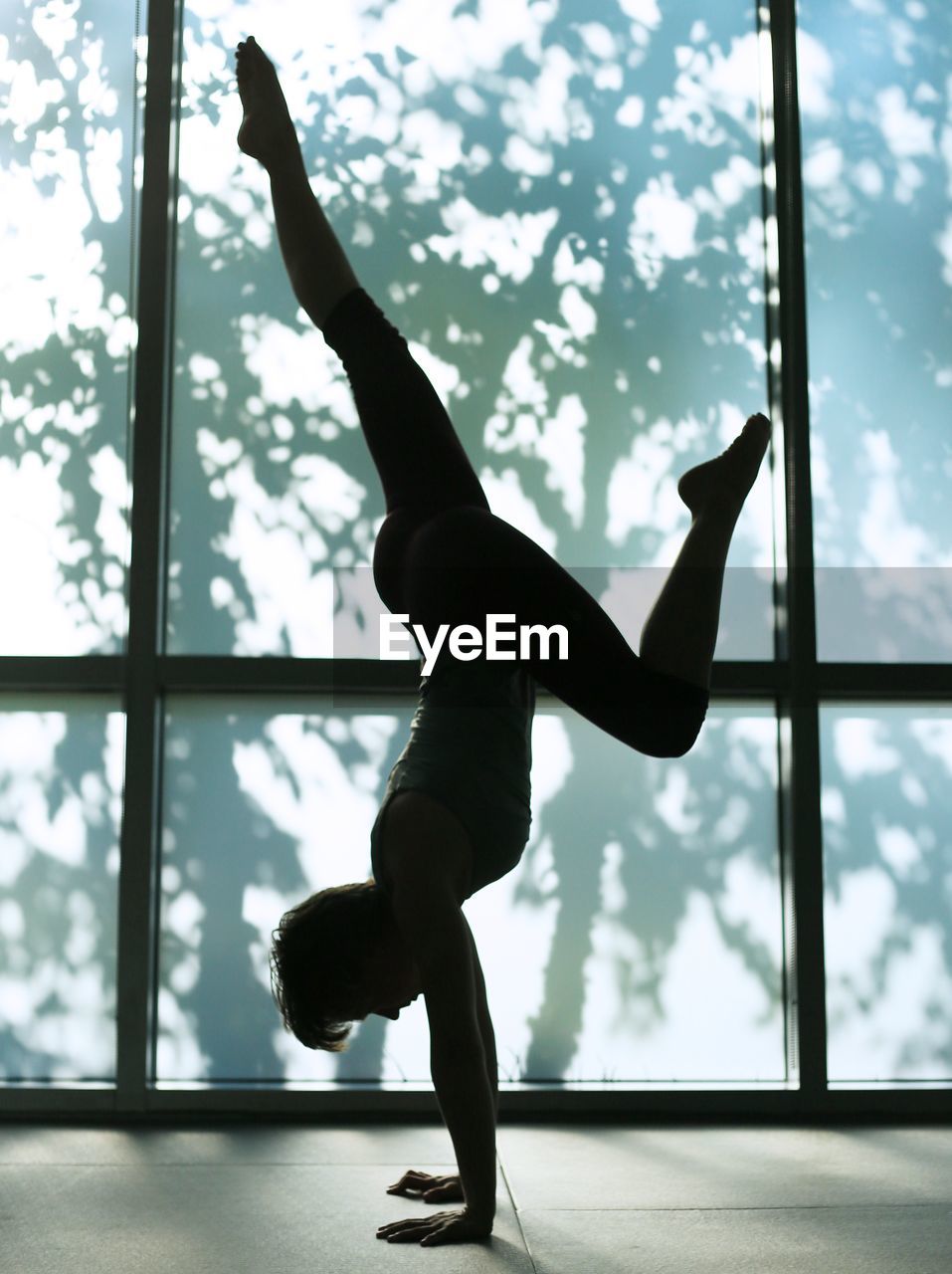 Side view of woman practicing handstand by window