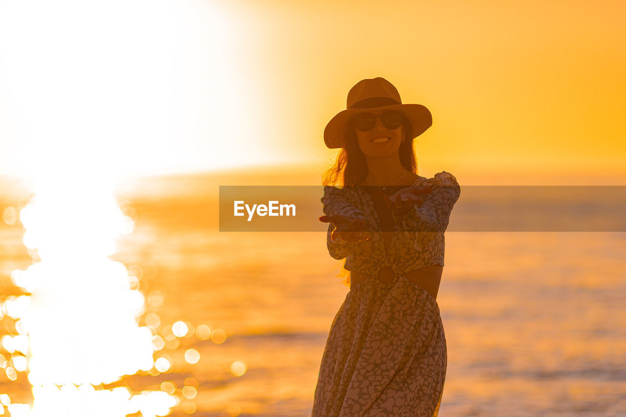 rear view of woman standing against orange sky during sunset