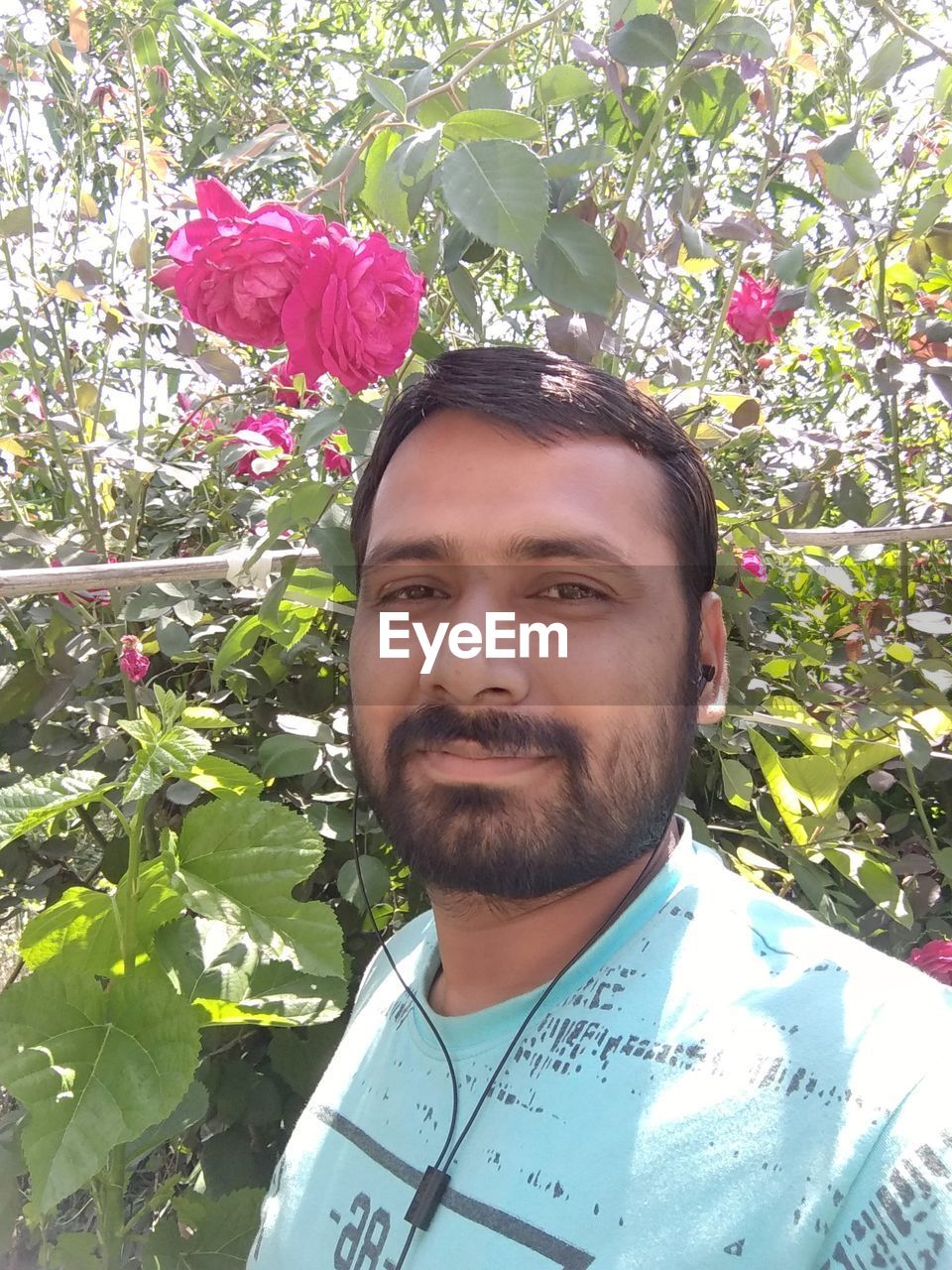 PORTRAIT OF YOUNG MAN WITH RED FLOWER IN PARK