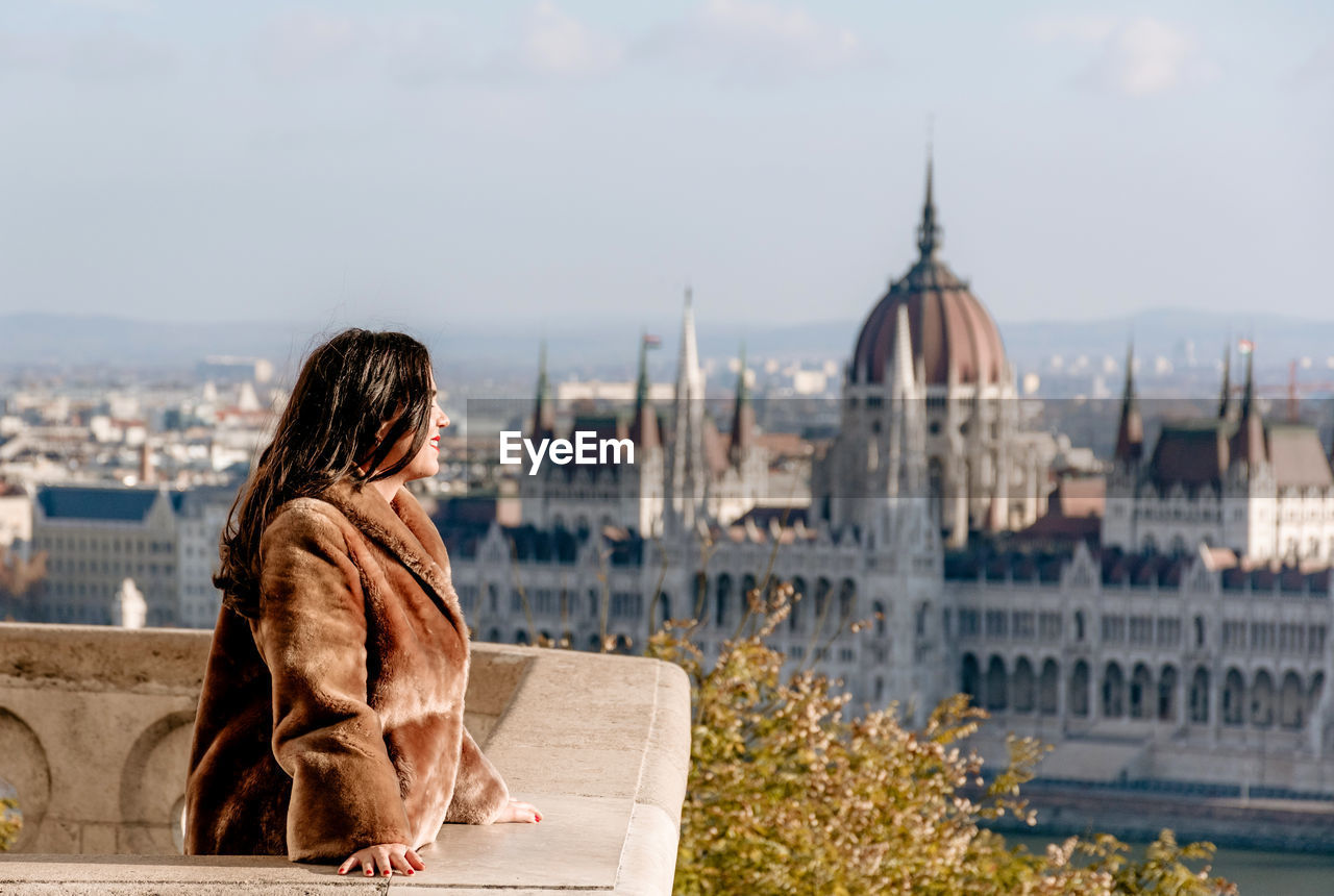 Young woman on balcony overlooking hungarian parliament in budapest, hungary