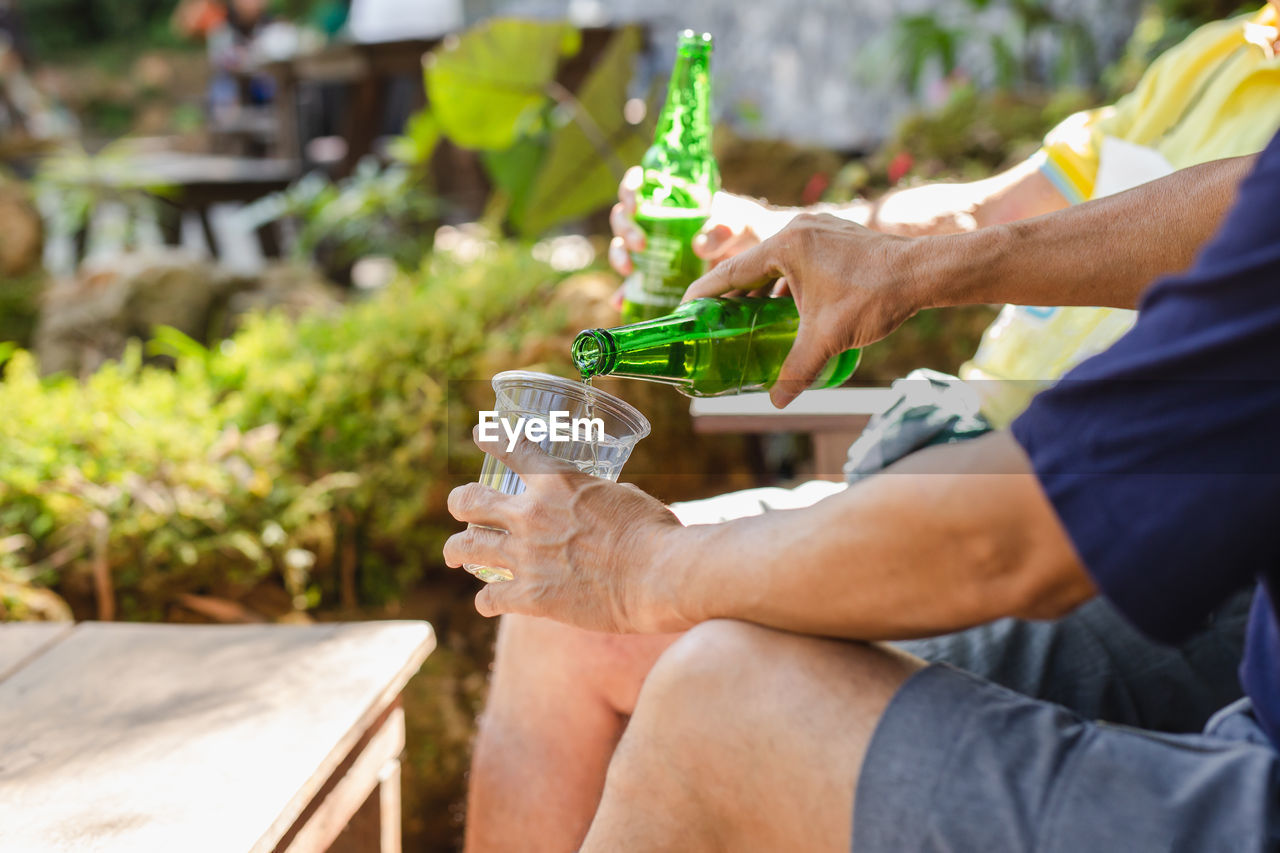 Man pouring beer in plastic glass from bottle during vacation.