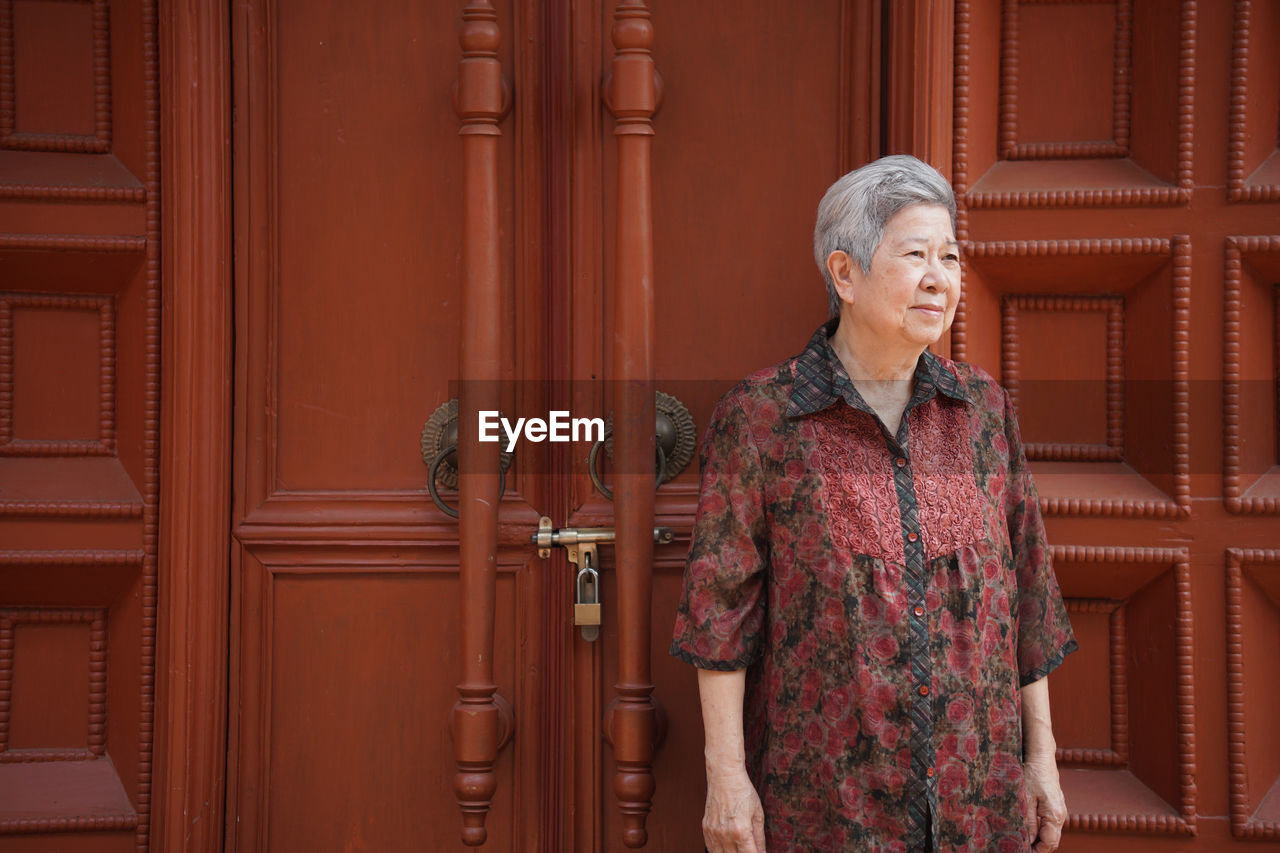 Senior woman standing against door