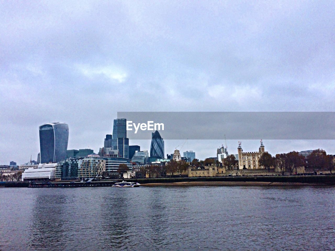 Thames river by modern buildings in city against sky