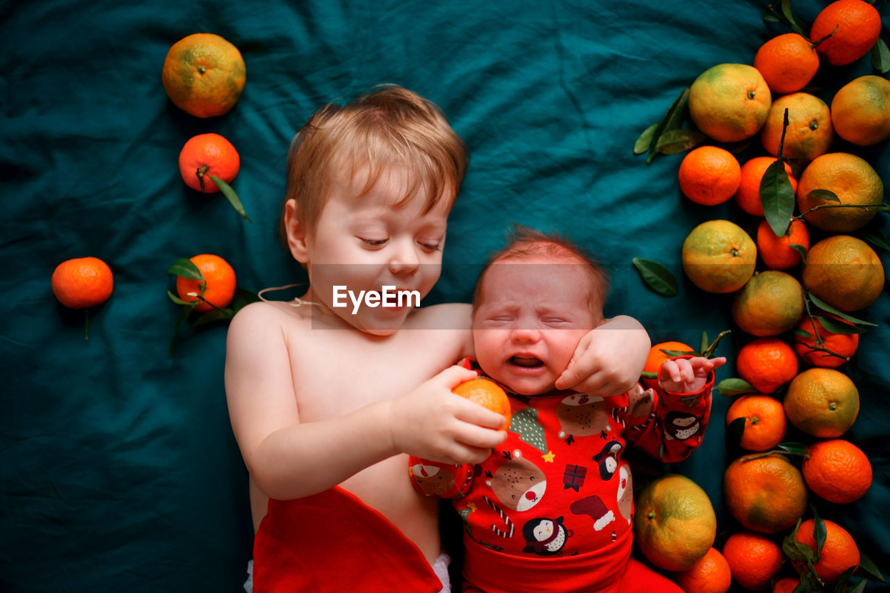 The older brother wants to feed the christmas newborn baby a tangerine, the baby cries.