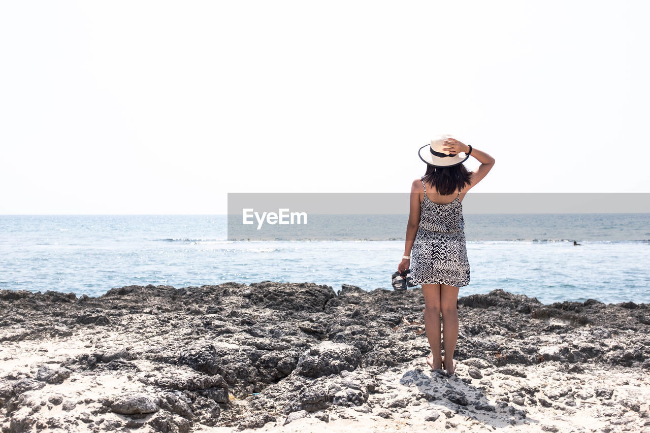 Rear view of young woman standing at beach against clear sky