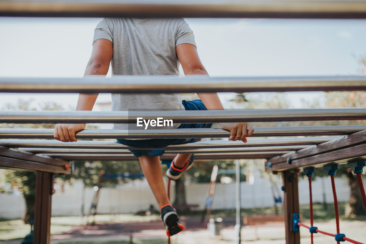 Low section of man sitting on monkey bars in playground