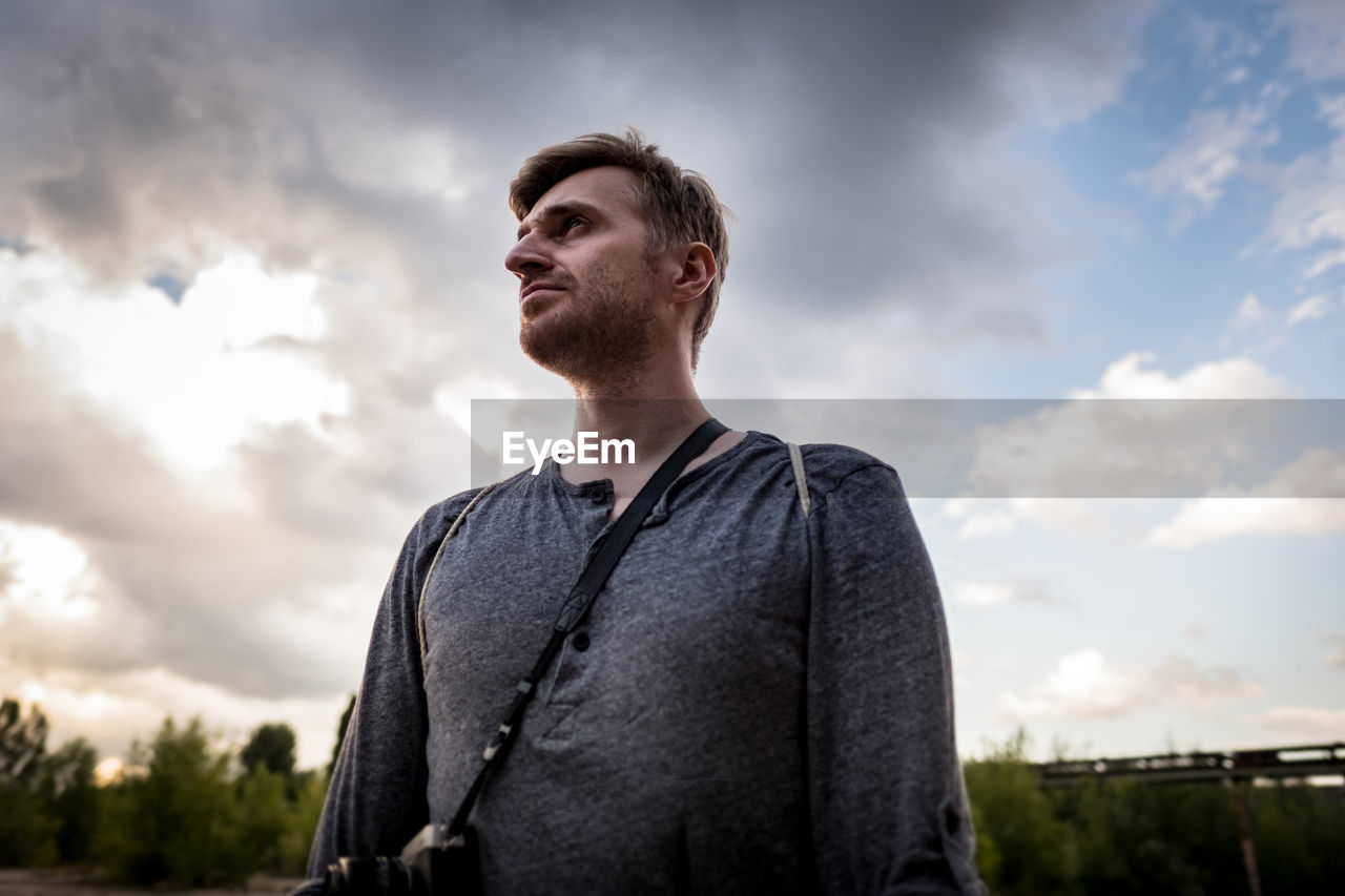 Low angle view of young man with camera against cloudy sky