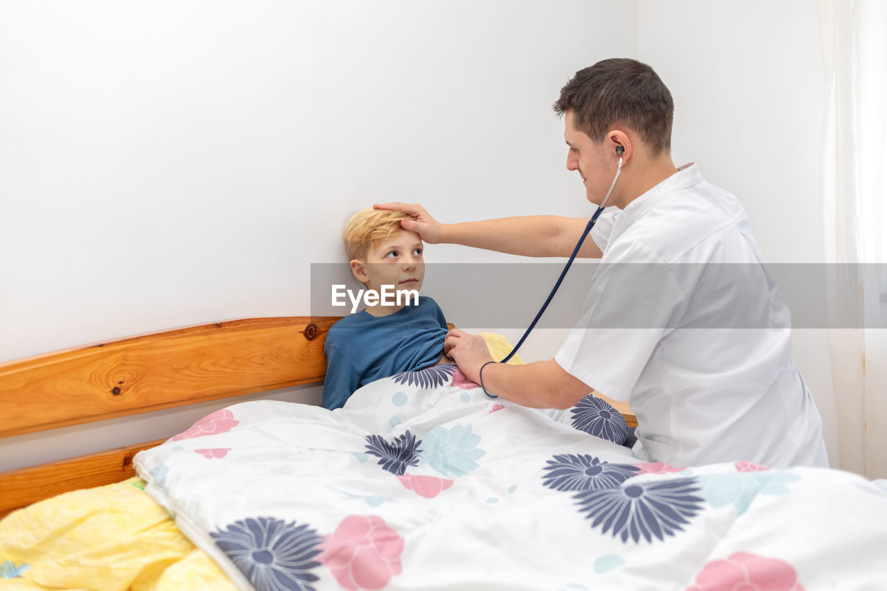 Doctor examining boy while sitting against wall