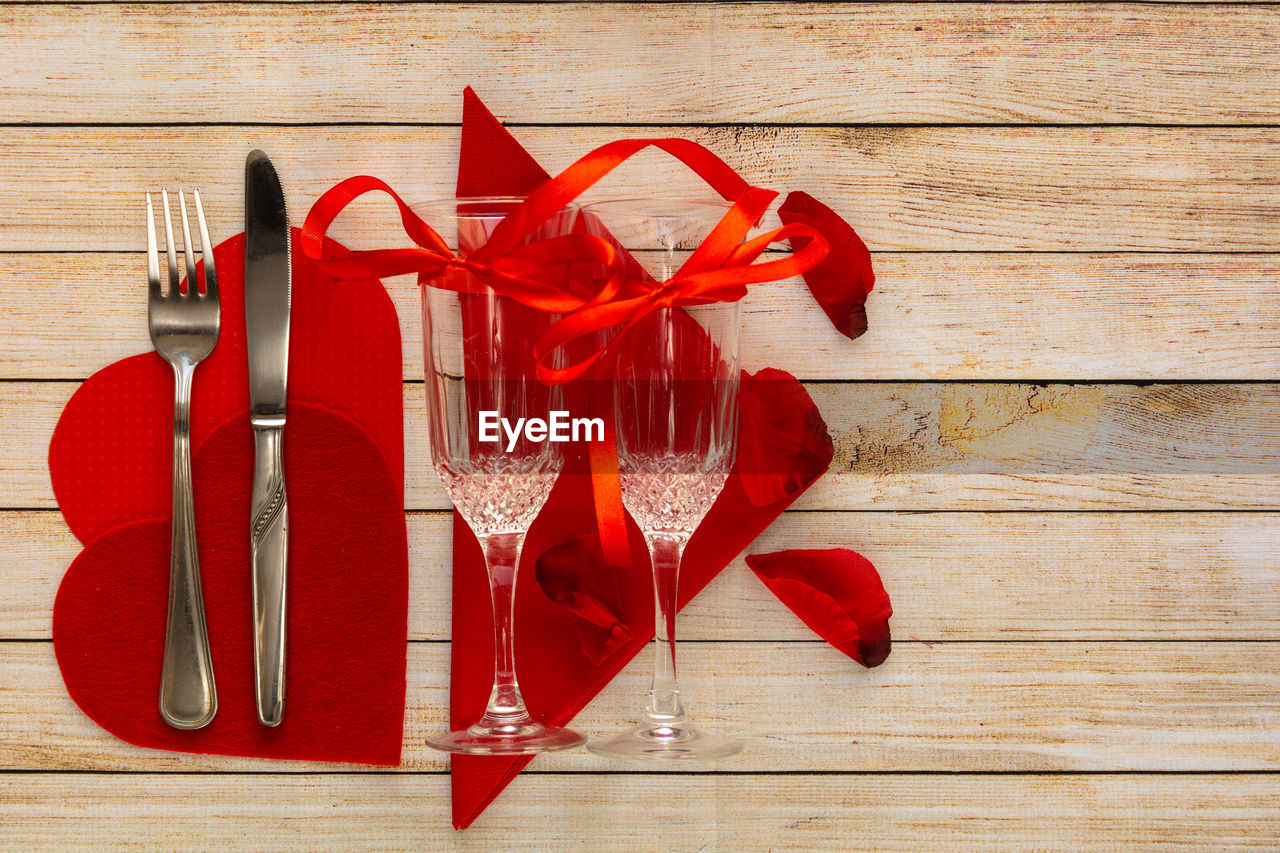 Wooden background with glasses of champagne, petals, hearts and cutlery.