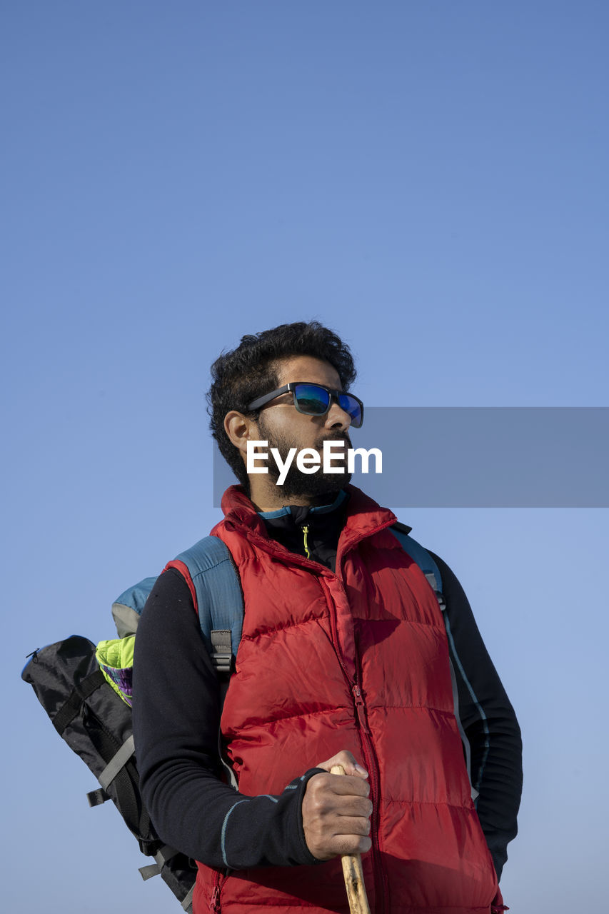 Portrait of an young indian traveler ready for hiking wearing red snow jacket and a backpack.freedom