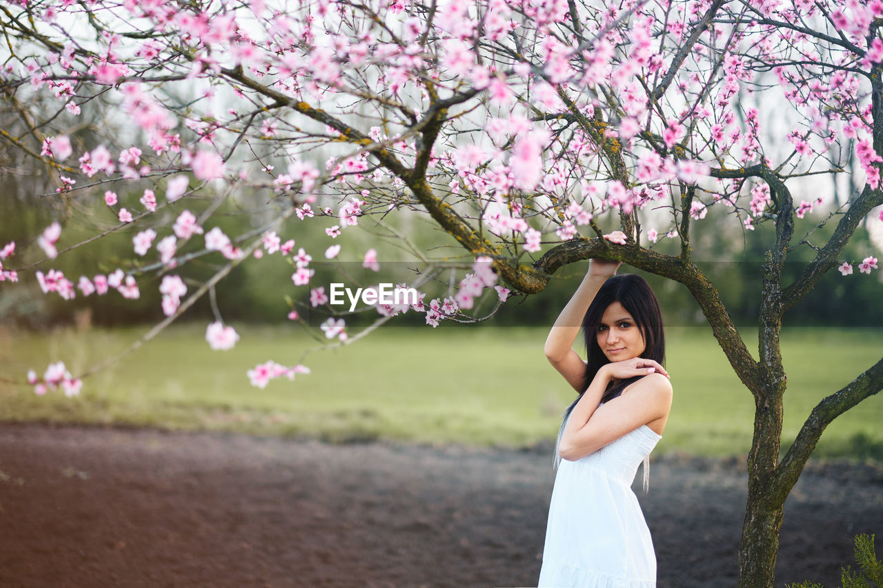 Young woman standing below pink flowers