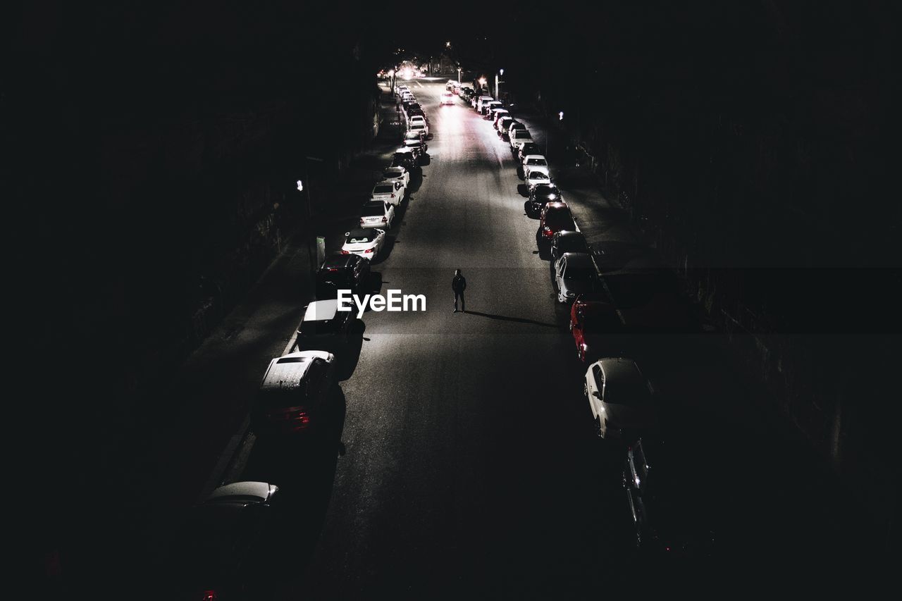 High angle view of man standing on street amidst cars at night