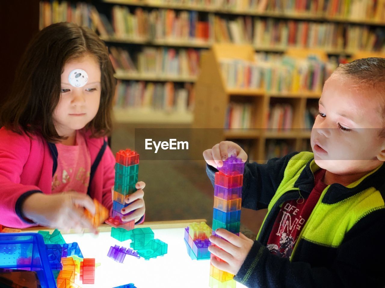 Siblings playing with toy blocks on table in library