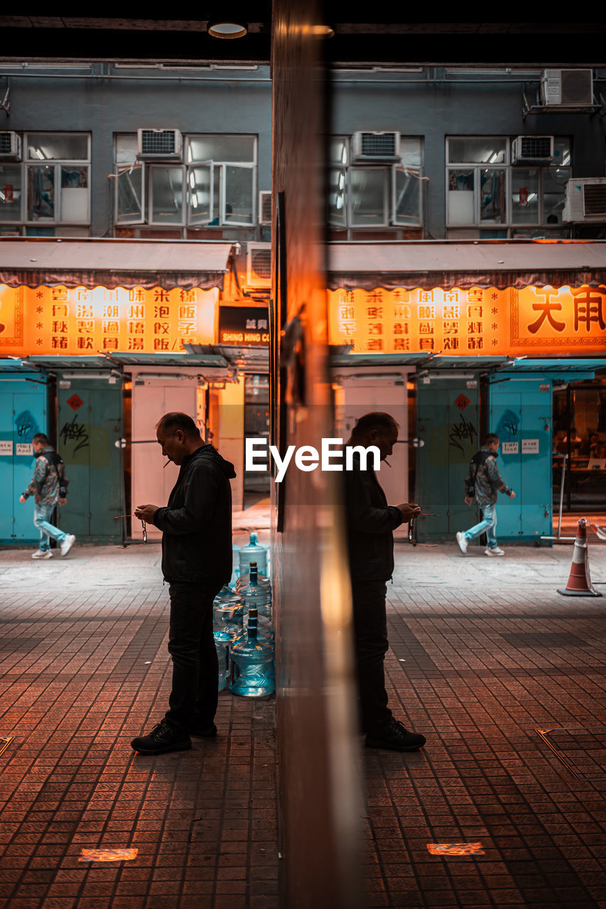 night, architecture, full length, city, adult, men, street, urban area, building exterior, built structure, footpath, travel, illuminated, city life, business, standing, walking, road, evening, transportation, store, outdoors, two people, rear view