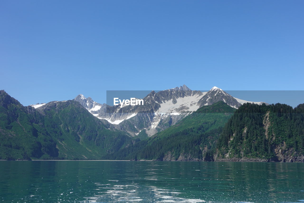 Scenic view of lake and snowcapped mountains against clear blue sky