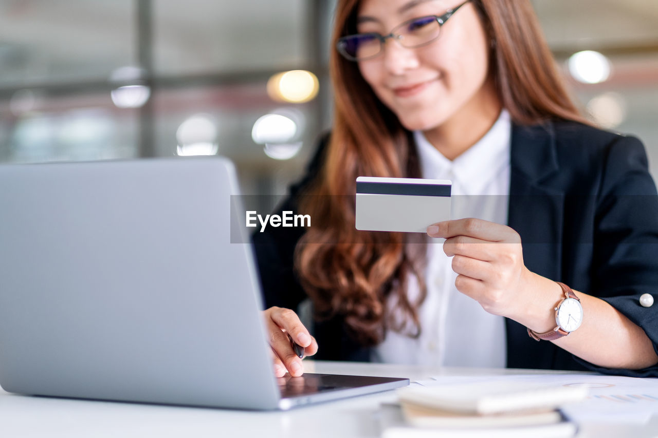 Mid adult woman using laptop while holding credit card over table