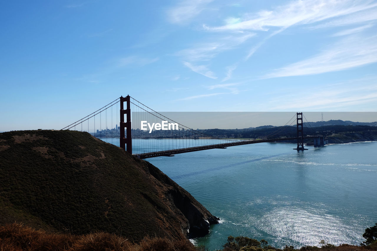 VIEW OF SUSPENSION BRIDGE OVER SEA AGAINST CLOUDY SKY