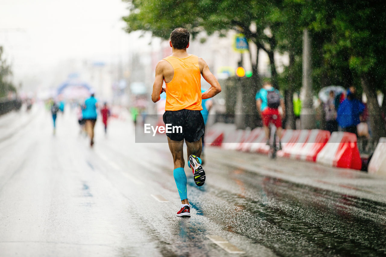 Back runner athlete run in rain on road city marathon