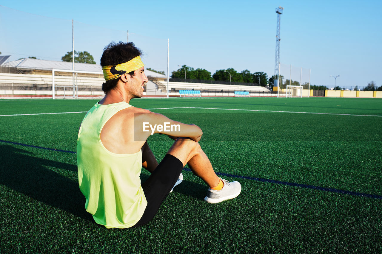 Young guy in sportswear looks at the horizon sitting on the grass