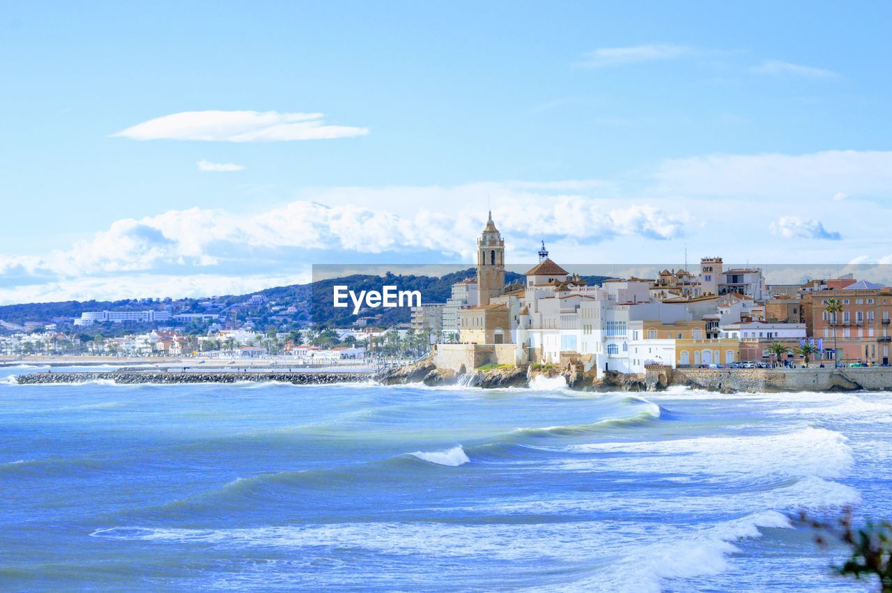 Buildings in sea against cloudy sky