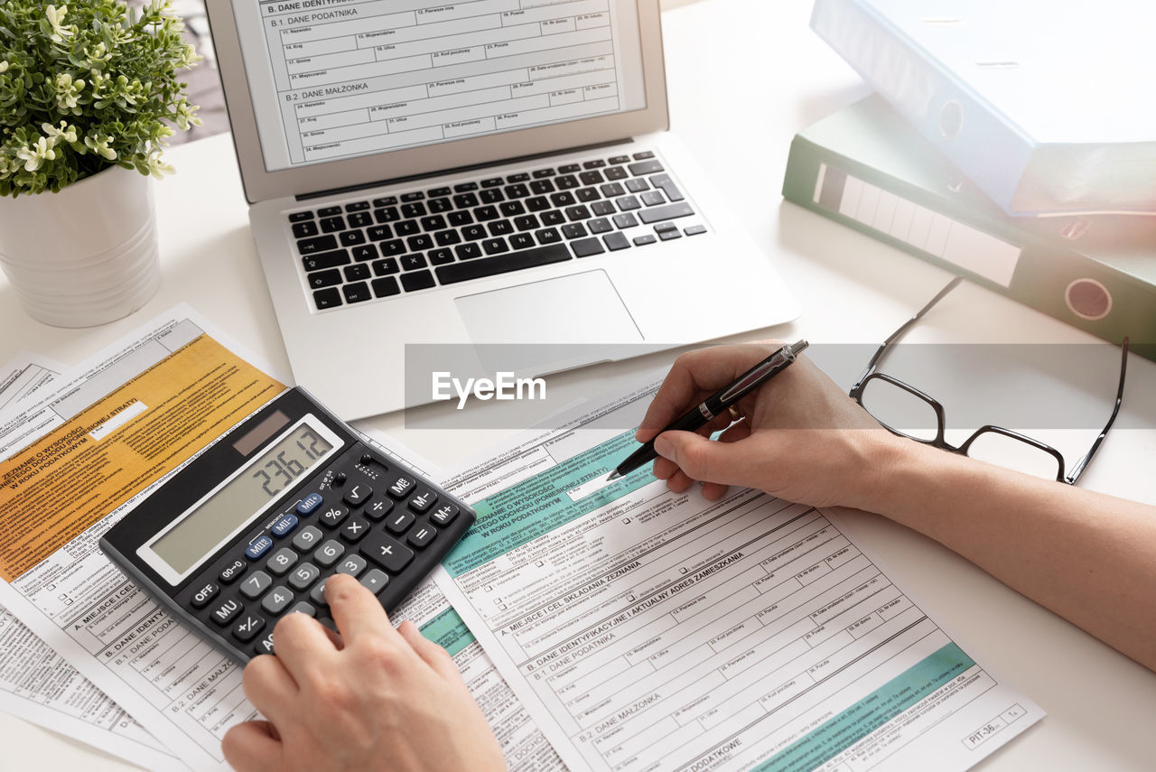 computer, wireless technology, technology, communication, laptop, adult, business, hand, writing, table, furniture, desk, working, document, one person, using laptop, business finance and industry, office, office equipment, computer equipment, high angle view, computer keyboard, indoors, finance, occupation, keyboard, women, paper, internet, portable information device, office supplies, pen, young adult, computer network, typing, businesswoman, place of work, learning, planning, smartphone, computer monitor, finance and economy