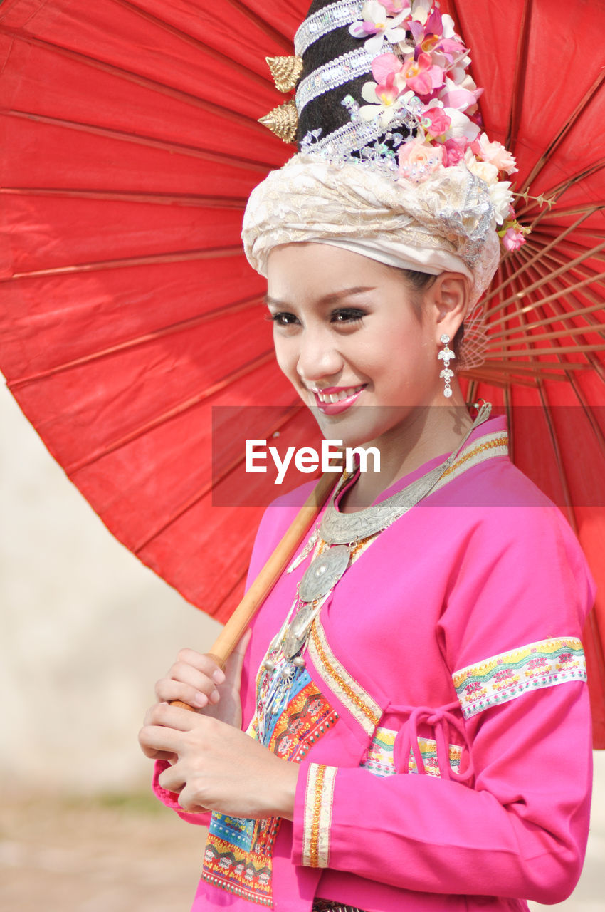 Happy young woman wearing traditional clothing while holding paper umbrella
