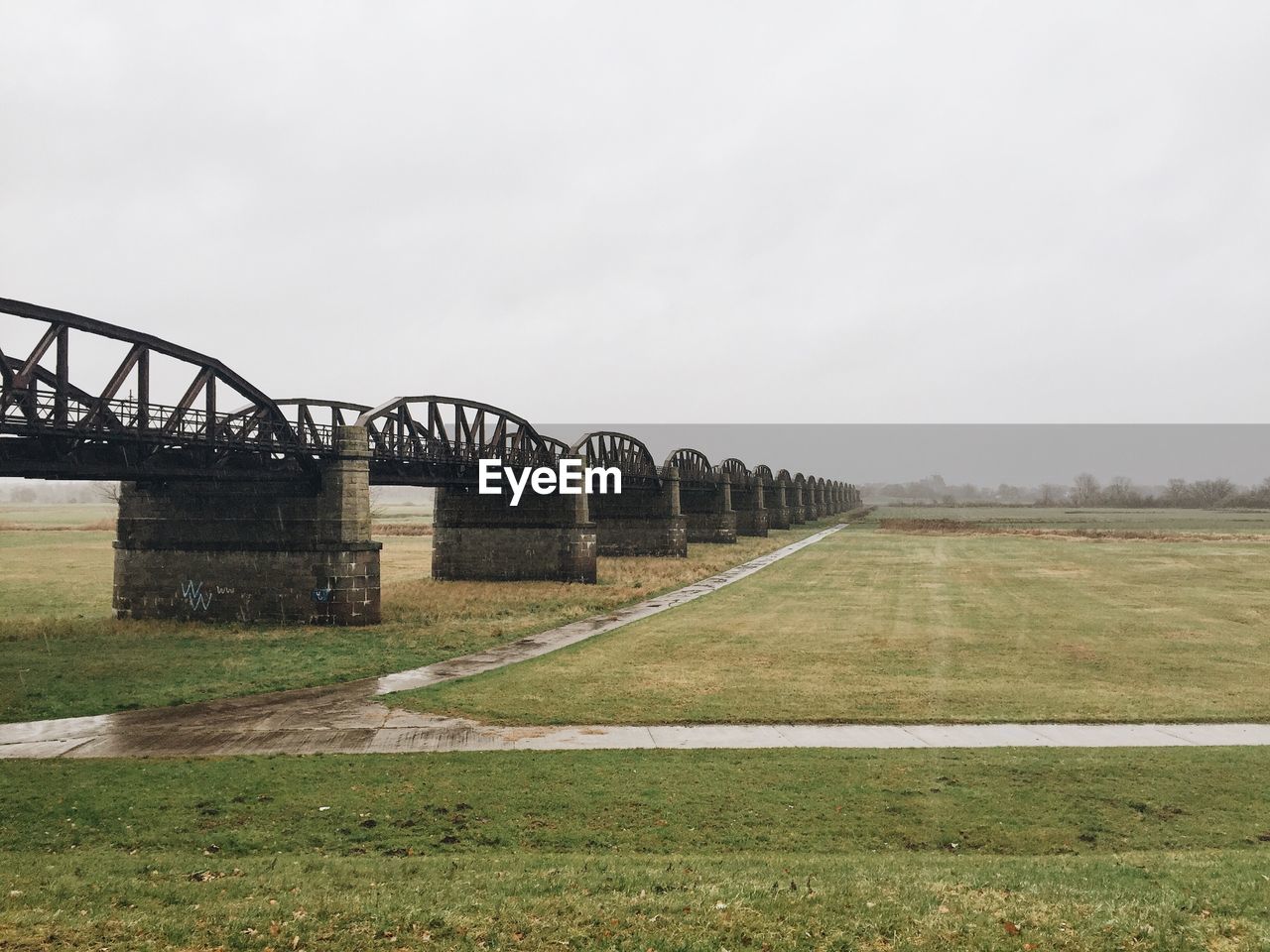 Old bridge over grassy field against clear sky