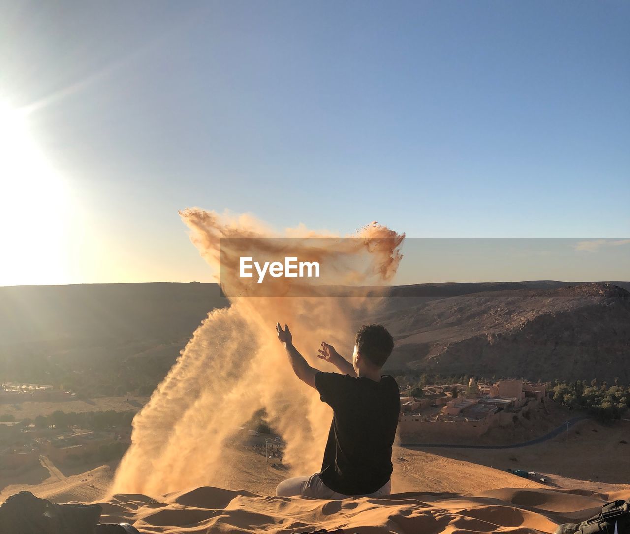 Man playing with sand while sitting on dessert against sky