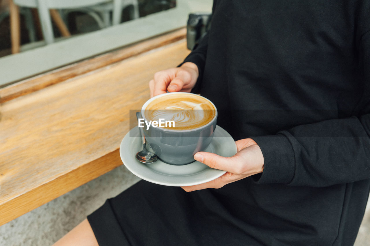 MIDSECTION OF MAN HOLDING COFFEE CUP AT HOME